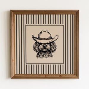 Könnte beinhalten: Ein gerahmter Kunstdruck mit einer Schwarz-Weiß-Illustration eines Hundes mit Cowboyhut. Das Kunstwerk befindet sich vor einem beigefarbenen Hintergrund mit einem schwarzen Rand, und der Rahmen hat eine braune Holzoptik. Der äußere Rahmen hat ein Streifenmuster.