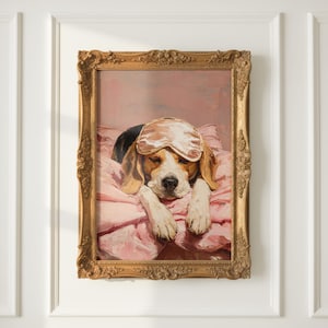 May include: A framed oil painting of a beagle dog resting on a pink pillow. The dog has brown, black, and white fur and wears a light pink sleep mask over its eyes. The frame is ornate, metallic gold, and features detailed floral carvings.