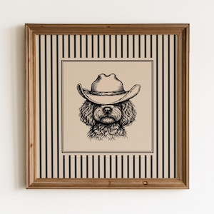 Könnte beinhalten: Ein quadratisches Wandbild mit einem schwarzen Tusche-Illustrationsdruck eines lockigen Hundes mit Cowboyhut. Das zentrale Motiv befindet sich auf einem beigen Hintergrund, umgeben von einem Rand aus vertikalen schwarzen Streifen in einem Holzrahmen.