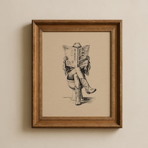 May include: A framed wall art print featuring a black ink line drawing of a figure wearing a cowboy hat and boots, sitting on a toilet whilst reading a newspaper. The artwork is set against a tan background and enclosed in a brown wooden frame.