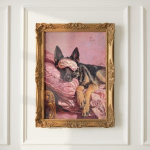 May include: A framed painting depicting a German Shepherd dog wearing a pink sleep mask, resting on a pink pillow. The dog is black and tan, and the painting is in an ornate gold frame. The background is a soft pink.