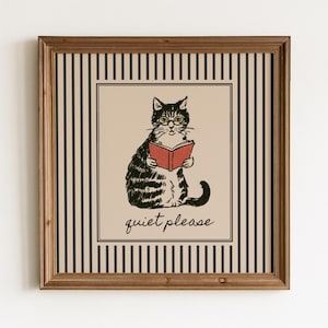 Könnte beinhalten: Ein quadratisches gerahmtes Wandbild mit einer schwarz-weißen Illustration einer Katze, die eine Brille trägt und ein rotes Buch liest. Der Hintergrund zeigt vertikale schwarze Streifen auf beigem Grund, darunter steht der Text "quiet please".