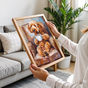 May include: A framed painting of a brown dog holding a white mug, seated in a brown armchair. The artwork has a light brown wooden frame. The painting's style is impressionistic, with visible brushstrokes and a warm colour palette.