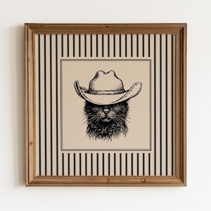 Könnte beinhalten: Ein quadratisches Wandbild mit einer schwarz-weißen Tuschezeichnung einer Katze mit Cowboyhut. Das zentrale Motiv befindet sich auf einem beigen Hintergrund mit einem schwarzen vertikalen Streifenmuster, eingefasst in einen Holzrahmen.
