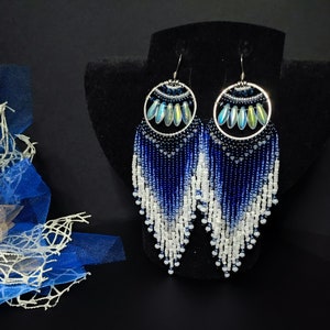 May include: A pair of long, beaded earrings with a blue and white ombre design. The earrings feature a silver hoop with iridescent blue beads.