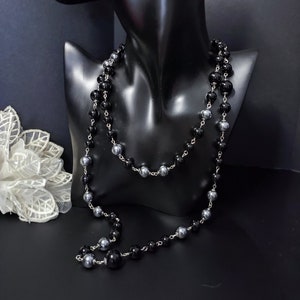 Peut inclure: Un long collier avec des perles noires et argentées. Le collier est superposé et a un design simple.