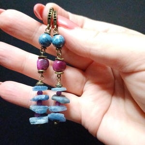 Peut inclure: Une paire de boucles d'oreilles longues et pendantes avec des perles de pierres précieuses bleues et roses et une finition bronze.