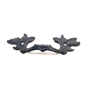 Op de afbeelding: Een donkergrijze, sierlijke trekker met een bloemmotief. De metalen hardware heeft een gebogen handvat en decoratieve uiteinden met bladachtige details. De trekker staat tegen een witte achtergrond.