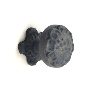May include: Black cast iron cabinet knob with a decorative floral design. The knob has a round shape and a star-shaped base.