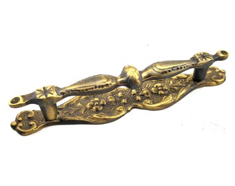 Pode incluir: Puxador de porta antigo em latão ornamentado com um design floral. A alça apresenta detalhes em forma de estrela e um design curvo e detalhado. O acabamento em latão confere-lhe um aspeto vintage, adequado para armários ou portas.