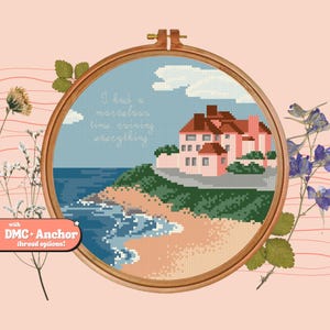 Op de afbeelding: Borduurpatroon van een roze huis op een klif met uitzicht op een blauwe zee met golven die breken op een zandstrand. De tekst "Ik had een geweldige tijd om alles te verpesten" is boven het huis geborduurd.