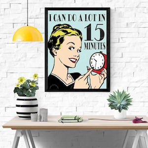 Puede incluir: Una impresión enmarcada de arte pop que presenta a una mujer señalando un despertador rojo. El texto dice: "I CAN DO A LOT IN 15 MINUTES". La mujer tiene el pelo rubio y lleva una blusa negra. El fondo es azul claro.