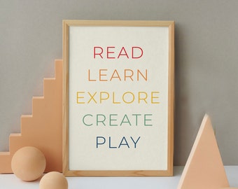 Könnte beinhalten: Ein gerahmter Druck mit den Worten "READ LEARN EXPLORE CREATE PLAY" in einem Regenbogen-Farbschema. Der Druck ist auf weißem Hintergrund und in einem hellen Holzrahmen gerahmt. Der Druck liegt auf einem Tisch mit einigen Dekorationsgegenständen.
