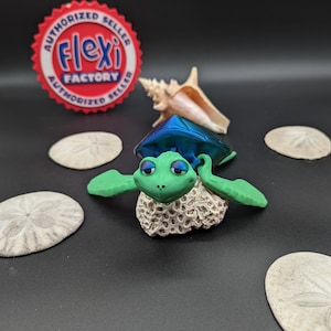 May include: A green and blue turtle figurine with large eyes and a shell that resembles a gemstone. The turtle is sitting on a white coral-like base. The figurine is surrounded by four sand dollars.