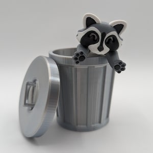 May include: A small gray trash can with a lid and a raccoon figurine peeking out of the top.