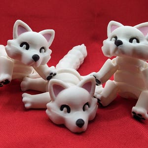 May include: Three white articulated toy foxes with black eyes and noses. The foxes are in various poses, with one lying down and the other two sitting up.