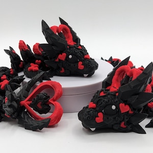 May include: Three black and red 3D printed dragon figurines with hearts. The dragons have detailed scales and are posed in different positions.