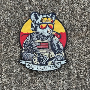 May include: A gray mouse wearing a military uniform and sunglasses with the text "R.A.T. Ready Airman Trained" on a yellow and red background.