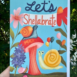 May include: Greeting card with a blue background featuring the text "Let's Shellabrate". The card has illustrations of snails, flowers, and balloons. The snails are on a mushroom.
