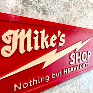 May include: A red wooden sign with a white lightning bolt and the text "Mike's Shop Nothing but HEAVY DUTY" in white lettering.