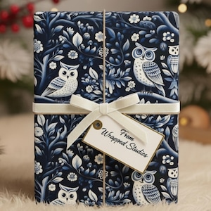 May include: A wrapped gift box featuring a navy blue owl and floral pattern. The gift is tied with a white ribbon and a tag that reads "From Wrapped Studies". The background includes candles and pinecones.
