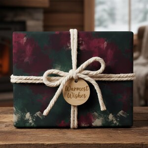 May include: A wrapped gift box with a dark green and burgundy abstract pattern. The box is tied with a white rope and a wooden tag that reads "Warmest Wishes". The gift is on a wooden table.