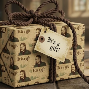 Op de afbeelding: Een ingepakte geschenkdoos met een bruine touwstrik en een label met de tekst "It's a gift!". Het inpakpapier heeft een herhalend patroon van een gezicht en de zin "It is a gift". Het cadeau staat op een stenen oppervlak.