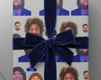 May include: A wrapped gift with a repeating pattern of a person's face on the wrapping paper. The gift is tied with a dark blue velvet ribbon and bow. The gift is on a white and light grey surface.