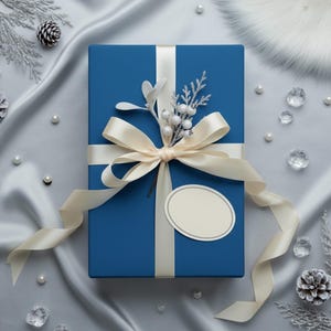 Op de afbeelding: Een blauwe geschenkdoos met een cr&egrave;mekleurig lint en strik, versierd met een takje witte bessen en zilveren accenten. De doos ligt op een zilveren satijnen doek, omringd door parels en kristallen.
