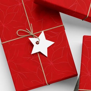 May include: Several red gift boxes with a floral pattern are arranged on a white surface. Each box is wrapped with twine and has a white tag attached. One tag is a star, and another is a heart. A ball of twine, scissors, and additional blank tags are also present.