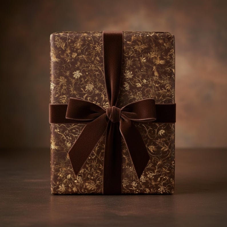 May include: A wrapped gift box with a brown floral pattern and a dark brown velvet ribbon tied in a bow. The wrapping paper has a gold floral design. The bow is centered on the front of the box.