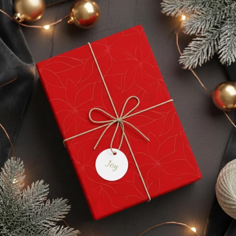 May include: A wrapped gift box with red floral patterned paper, tied with twine and a tag that says "Joy". The box is surrounded by Christmas ornaments and greenery.