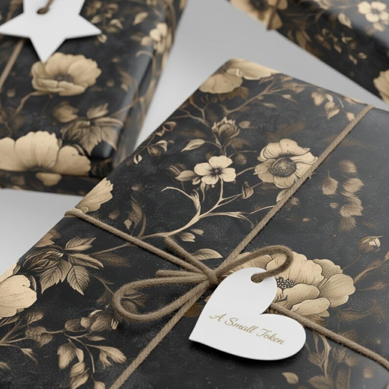 May include: Several wrapped gifts with black floral patterned paper and twine bows. The paper features a repeating pattern of beige flowers and foliage. A white heart-shaped tag with the text "A Small Token" is attached to one of the gifts.