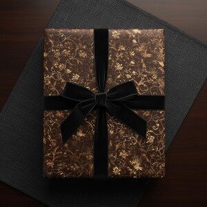 May include: A wrapped gift box with brown floral patterned paper and a black velvet ribbon and bow. The gift is presented on a dark gray textured surface and a dark brown wooden surface.