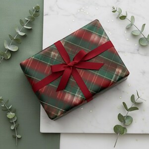 May include: A present wrapped in red and green tartan paper, secured with a burgundy ribbon and bow. The gift sits on a white marble surface, decorated with eucalyptus sprigs and star-shaped confetti.