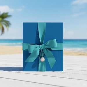 Op de afbeelding: Een blauwe geschenkdoos, vastgebonden met een turquoise lint en strik. Een kleine schelpenbedel hangt aan de strik. De achtergrond toont een strandsc&egrave;ne.