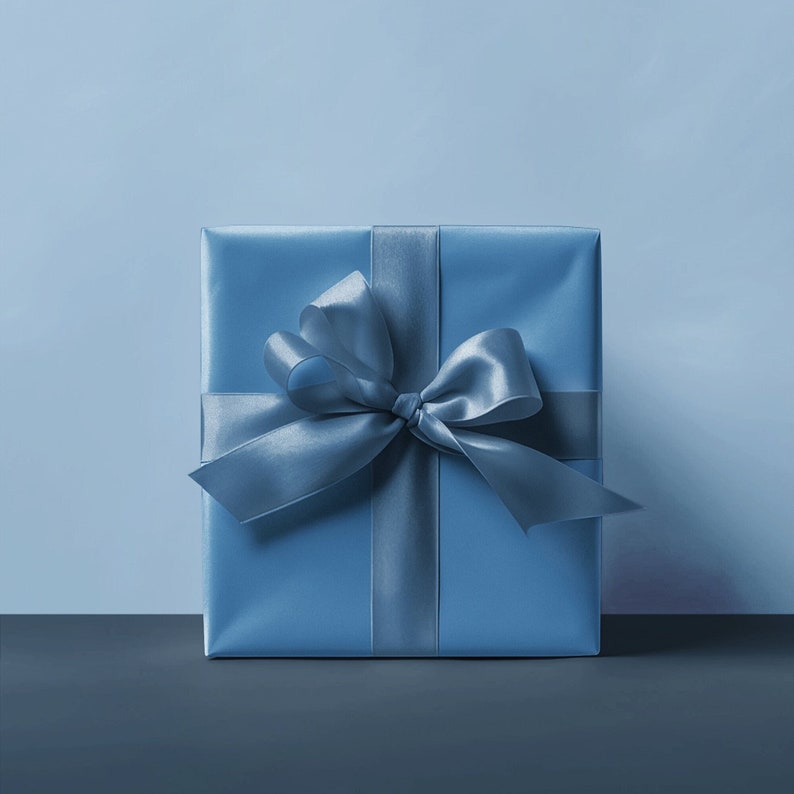 Op de afbeelding: Een vierkante geschenkdoos verpakt in blauw papier met een bijpassend satijnen lint en strik. De strik is gecentreerd op de voorkant van de doos en het lint loopt verticaal en horizontaal rond de doos.