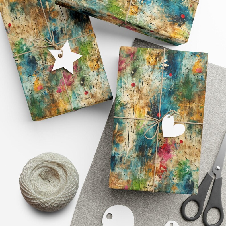 May include: Three gift boxes wrapped in colorful abstract patterned paper with twine and white paper star and heart shaped tags. The boxes are on a gray fabric surface with a ball of twine and a pair of scissors.