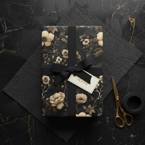 May include: A wrapped gift with floral patterned paper, tied with a black ribbon and bow. A small tag with the word "Love" hangs from the bow. Gold scissors and a spool of black twine are nearby.