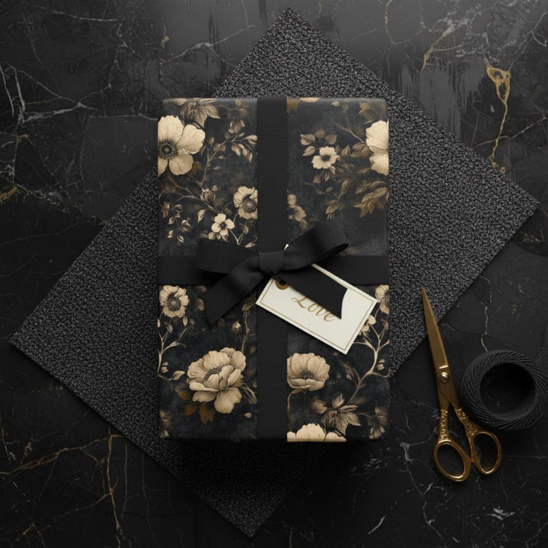 May include: A wrapped gift with floral patterned paper, tied with a black ribbon and bow. A small tag with the word "Love" hangs from the bow. Gold scissors and a spool of black twine are nearby.
