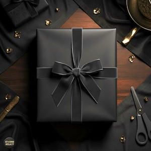 Op de afbeelding: Een zwarte geschenkdoos, gebonden met een zwart lint en strik. De doos staat op een houten oppervlak, omringd door zwarte stof, gouden accenten en een zwarte schaar. Het Studio Select logo is zichtbaar.