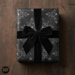 May include: A wrapped gift with black wrapping paper featuring a silver floral design. A wide black velvet ribbon and bow secure the package. The gift is presented on a dark wooden surface. The Studio Select logo is visible.