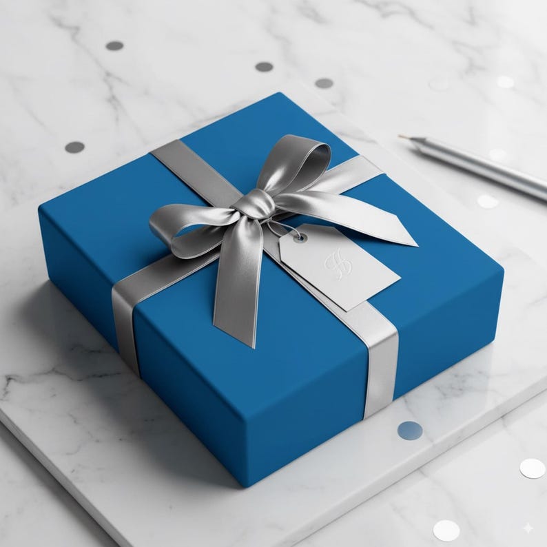 Op de afbeelding: Een blauwe geschenkdoos met een zilveren lint en strik. Een wit label hangt aan de strik. De geschenkdoos staat op een wit marmeren oppervlak met zilveren confetti.