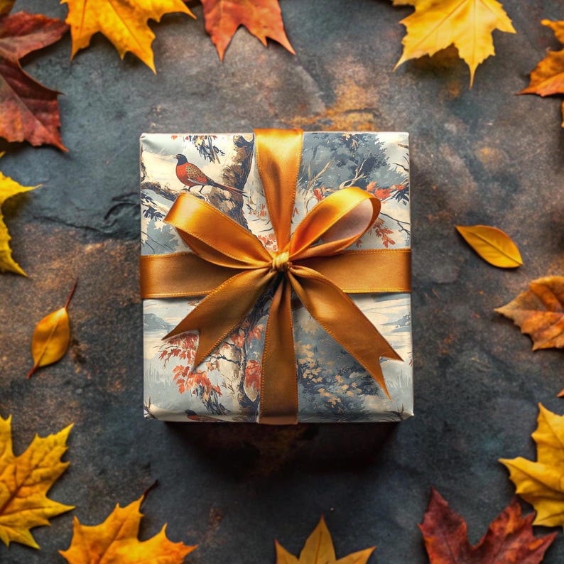 Op de afbeelding: Een cadeaudoos ingepakt in blauw en wit papier met een gouden lint en een vogelontwerp. De doos is omringd door herfstbladeren.