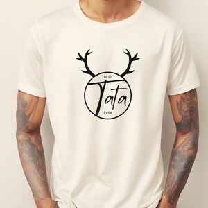 May include: White t-shirt with a black graphic design featuring a circle with the text "Best Tata Ever" and antlers above the circle.