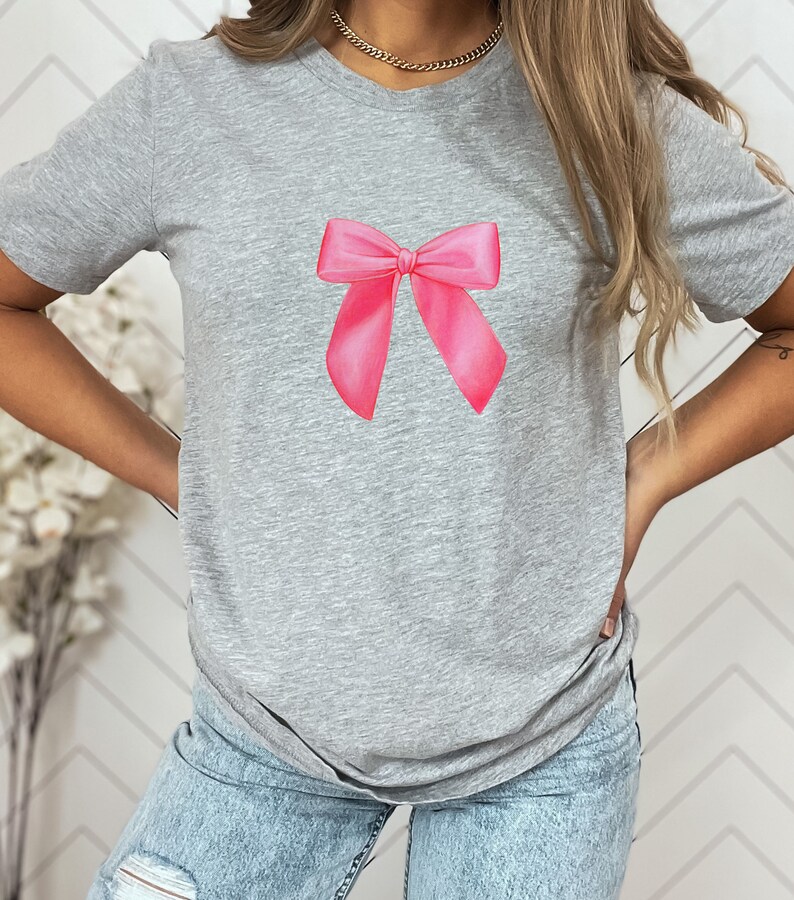 May include: A gray t-shirt with a pink bow printed on the front.