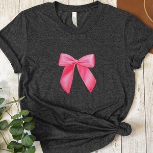 May include: A dark gray t-shirt with a pink bow printed on the front.