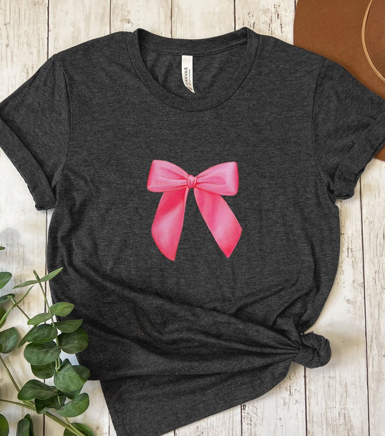 May include: A dark gray t-shirt with a pink bow printed on the front.