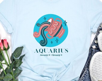 Puede incluir: Camiseta azul claro con un gráfico del signo zodiacal Acuario, un círculo azul con una jarra de agua rosa y negra vertiendo agua, y el texto "AQUARIUS January 20 - February 18".