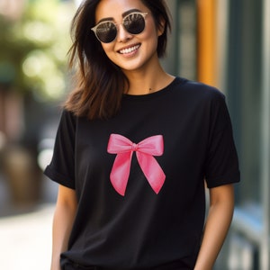 May include: A black t-shirt with a pink bow graphic on the front. The shirt has a crew neck and short sleeves.